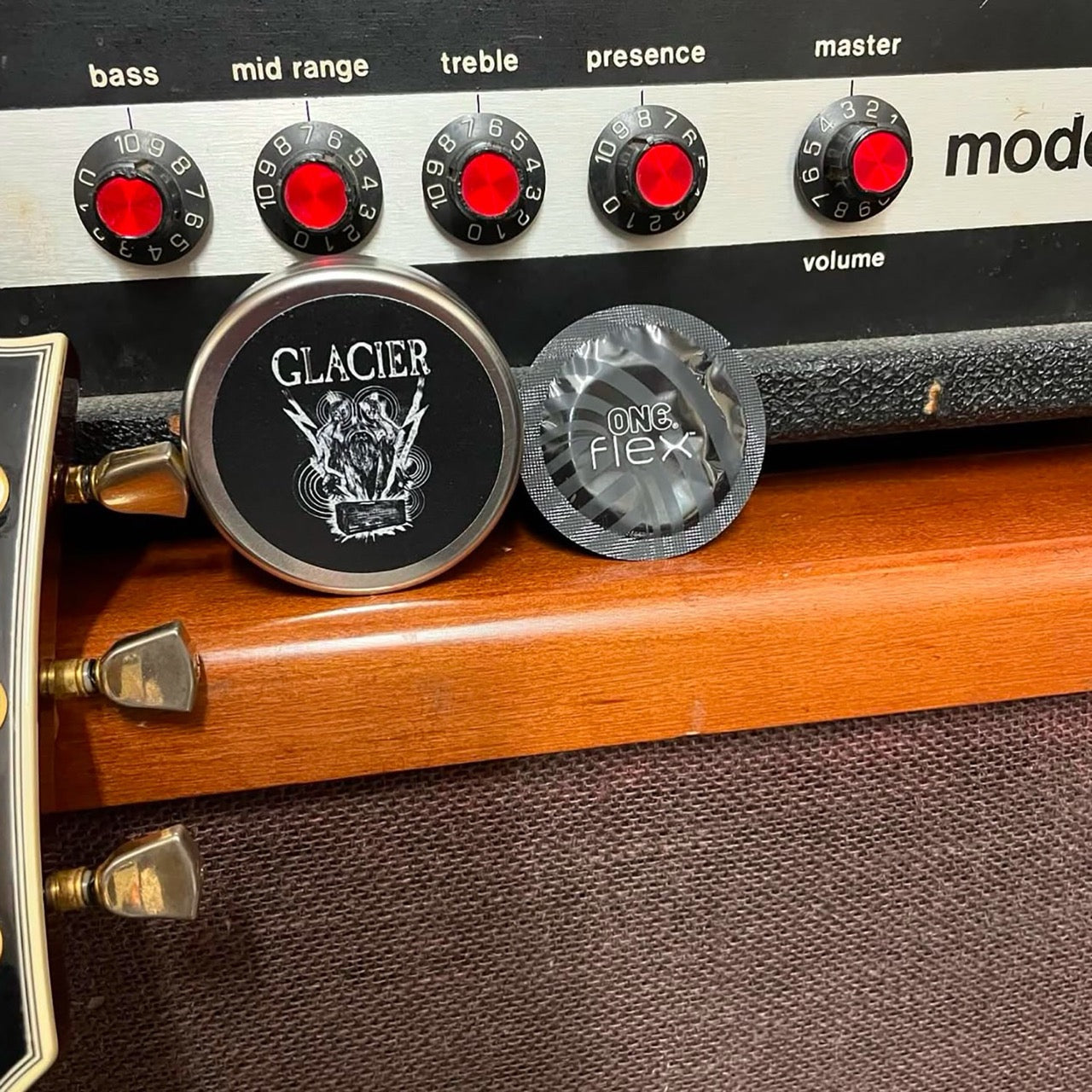 Image shows a ONE Flex condom and a Glacier printed condom tin propped up against a music machine. 